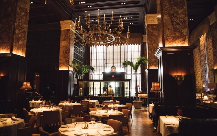Elegant restaurant interior with large chandelier, marble columns, and well-set tables with white linens.