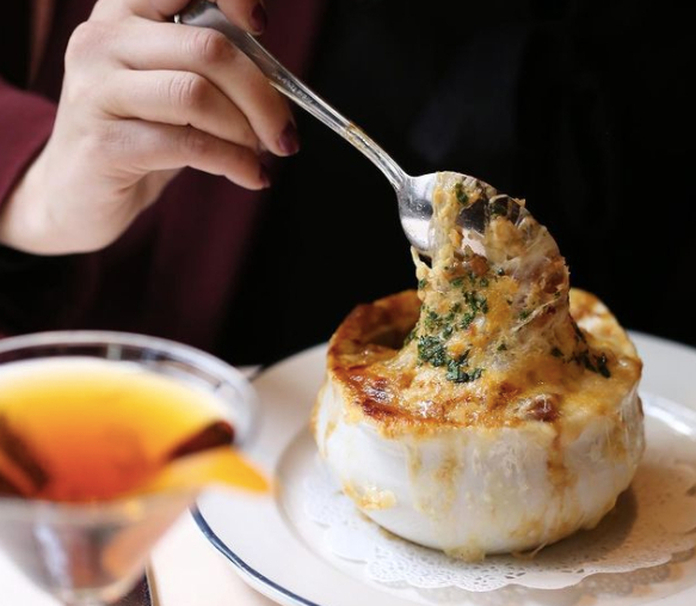 Person eating creamy soup from a baked garlic bowl with a spoon, served with a martini glass.